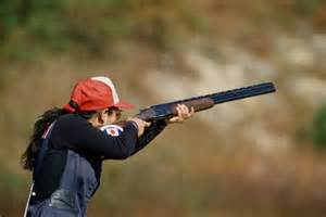 Woman shooting clay pigeon with a shotgun.